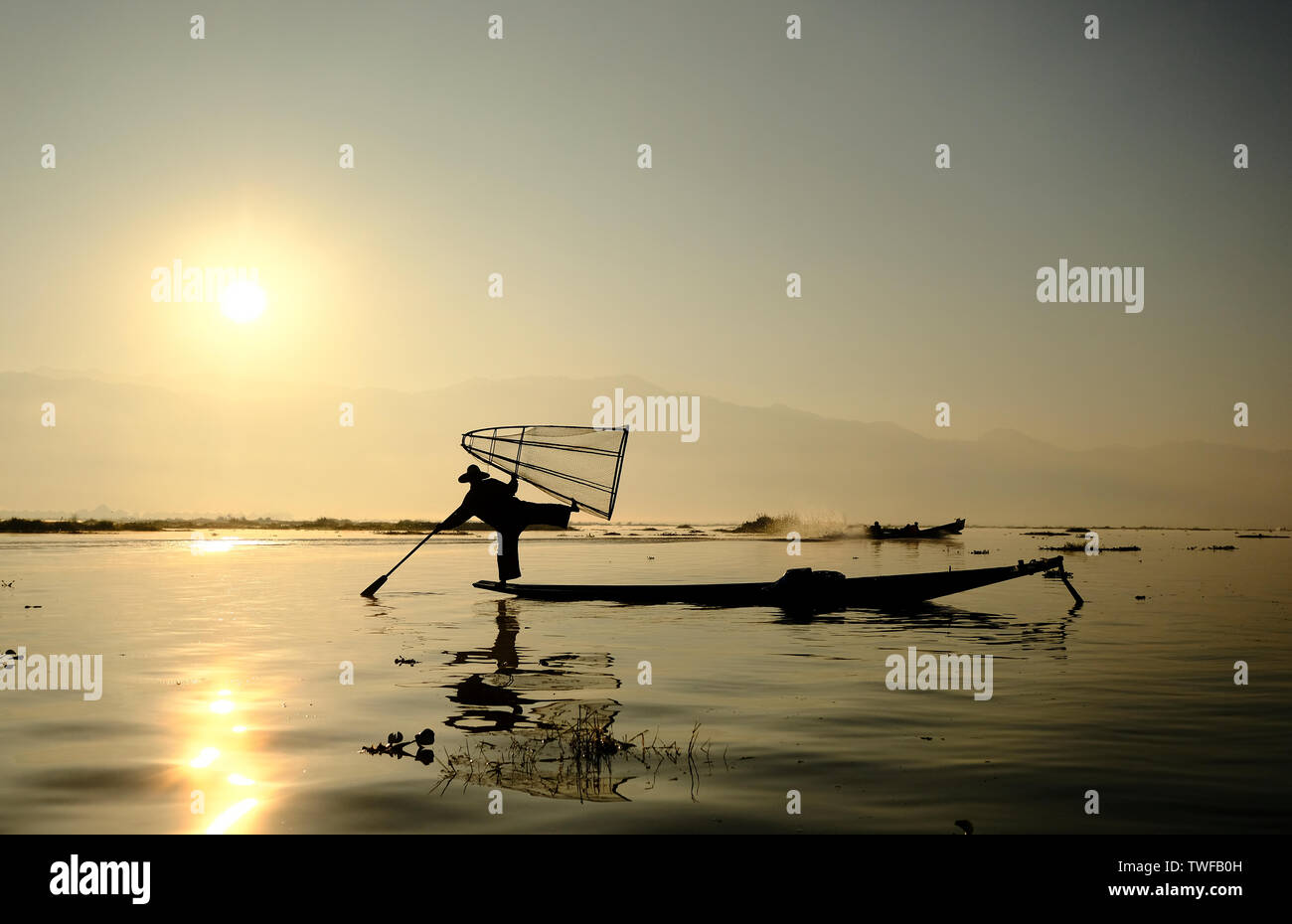 Locale pescatore Intha sul Lago Inle saldi su una gamba mentre paddling la sua canoa. Foto Stock