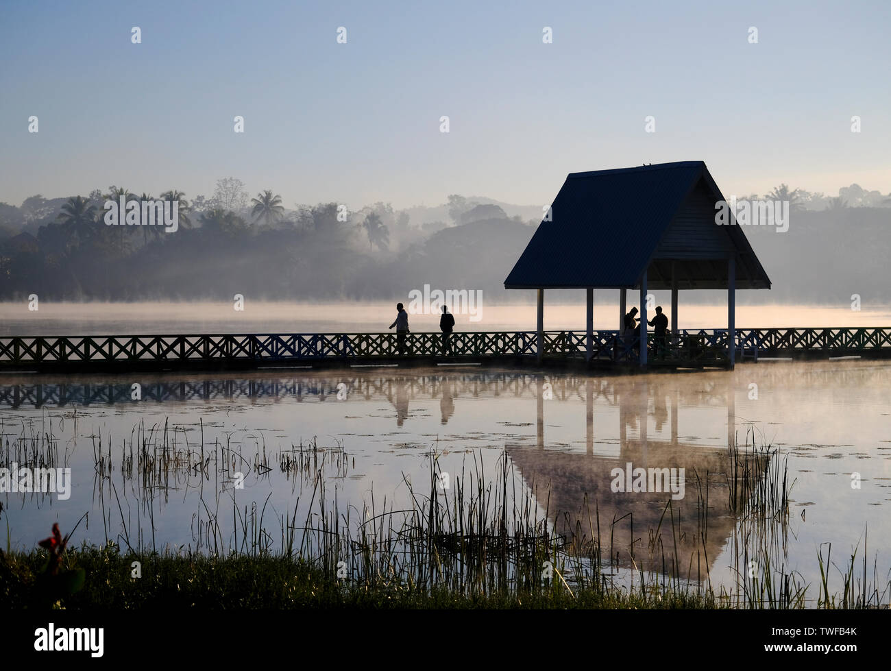 Le figure si stagliano contro alba la nebbia in aumento a un lago di Loikaw in Myanmar. Foto Stock