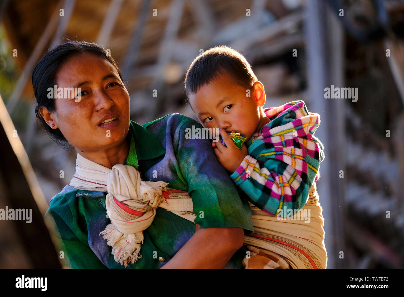 Una donna birmano e il bambino sulla schiena sono illuminate dal sole di sera in un villaggio rurale in Stato Kayah in Myanmar. Foto Stock