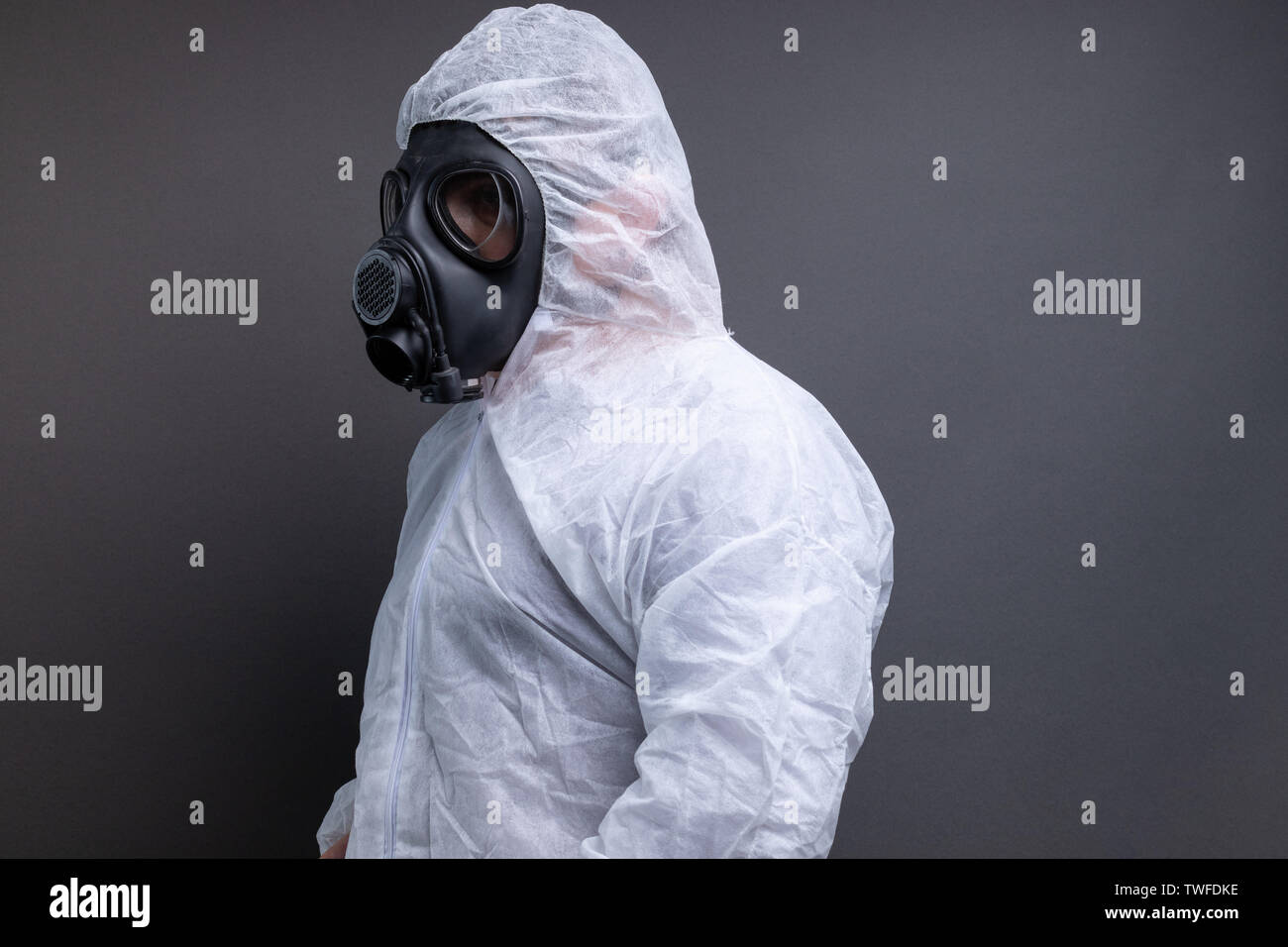 Vista laterale dell'uomo con maschera a gas in tuta protettiva tuta contro uno sfondo grigio Foto Stock