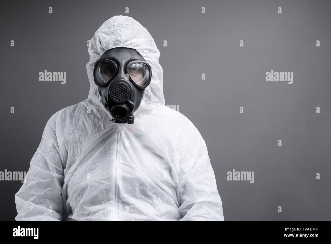 Uomo con maschera a gas in tuta protettiva tuta contro uno sfondo grigio Foto Stock