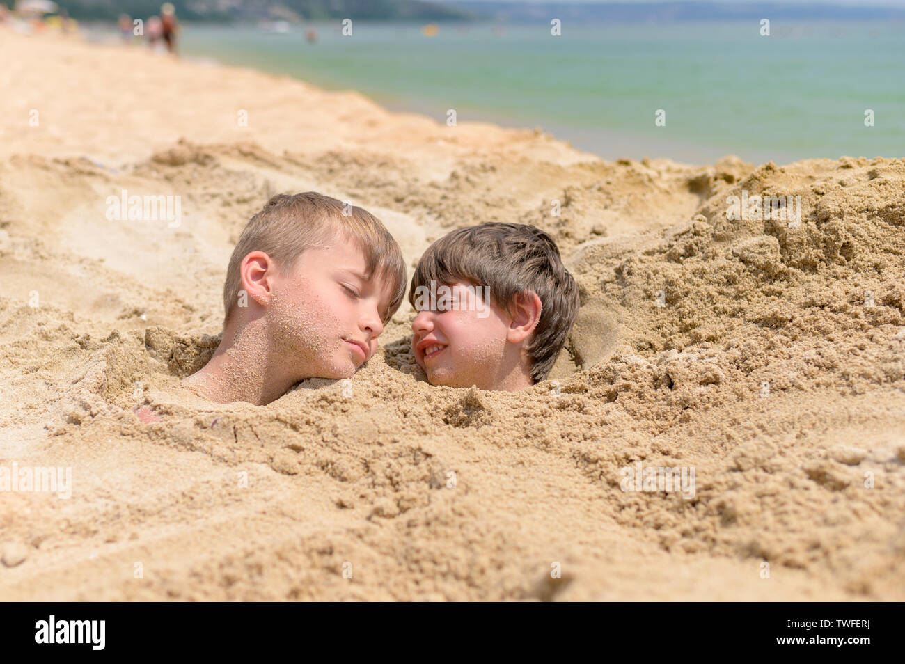 Carino kids sepolto nella sabbia sulla spiaggia, giorno di estate Foto Stock