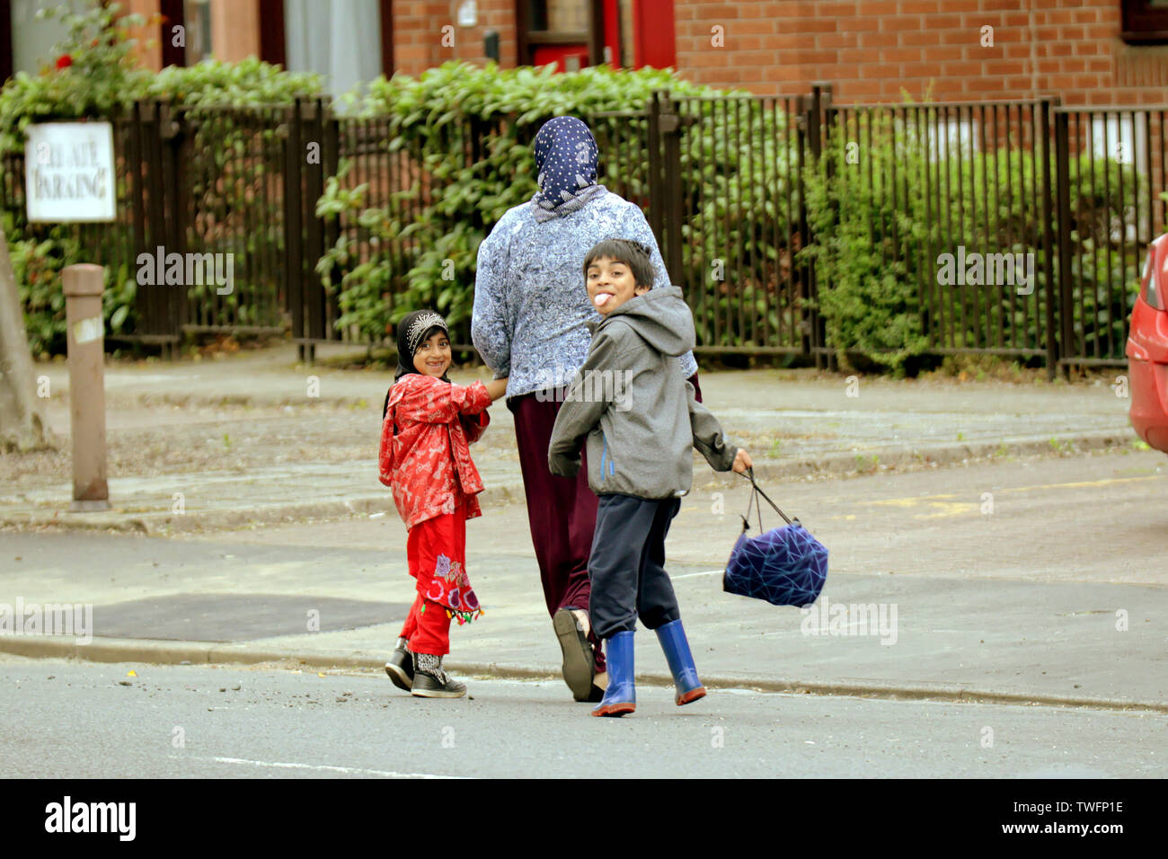Famiglia asiatica dei bambini che giocano in strada Govan camminare a casa da scuola con la madre sorridente Foto Stock