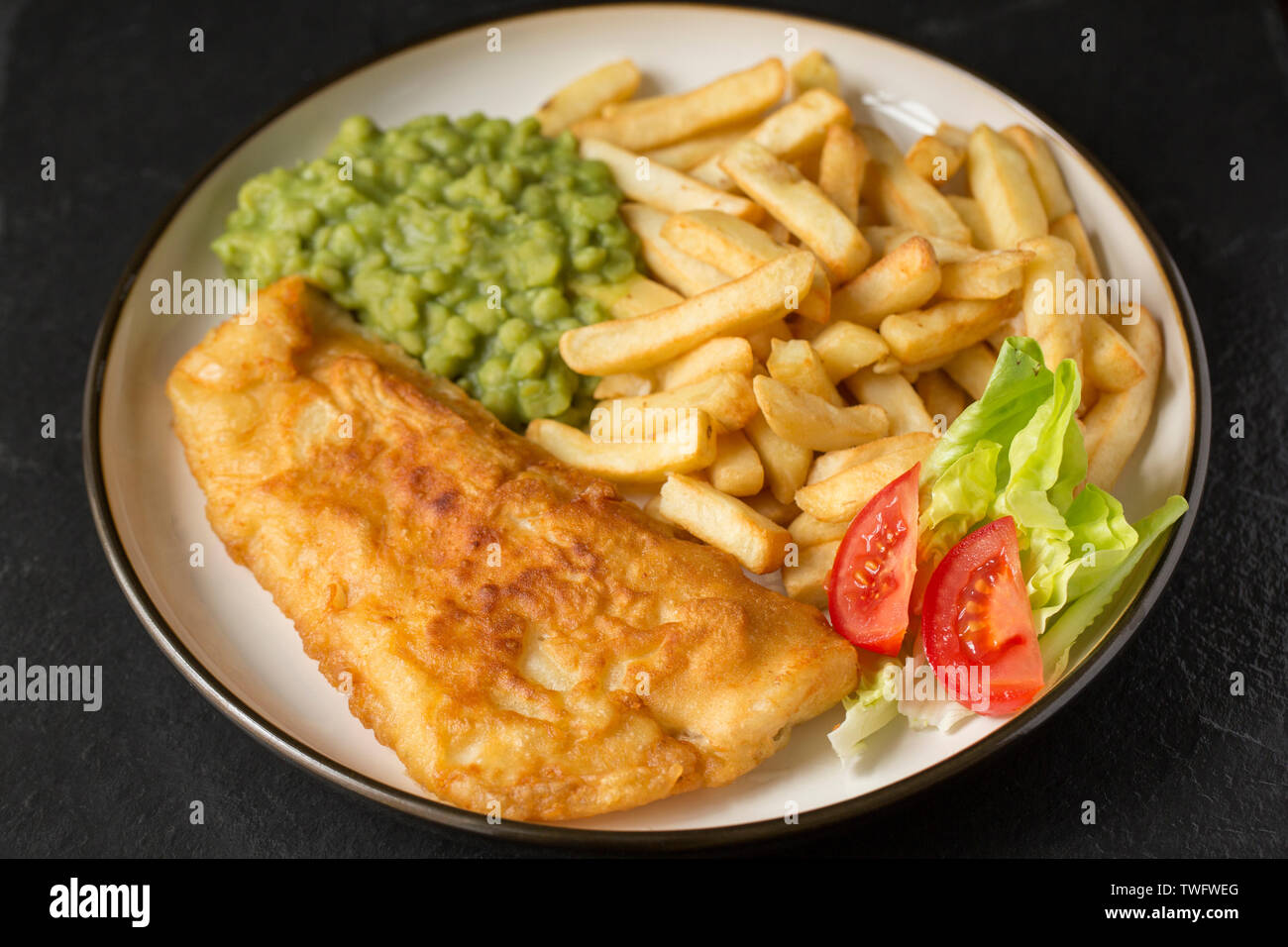 Un filetto di pollack, Pollachius pollachius, che è stato rivestito in casalingo pastella e fritti e serviti con fiacco piselli e patatine. Il pollack è stato Foto Stock