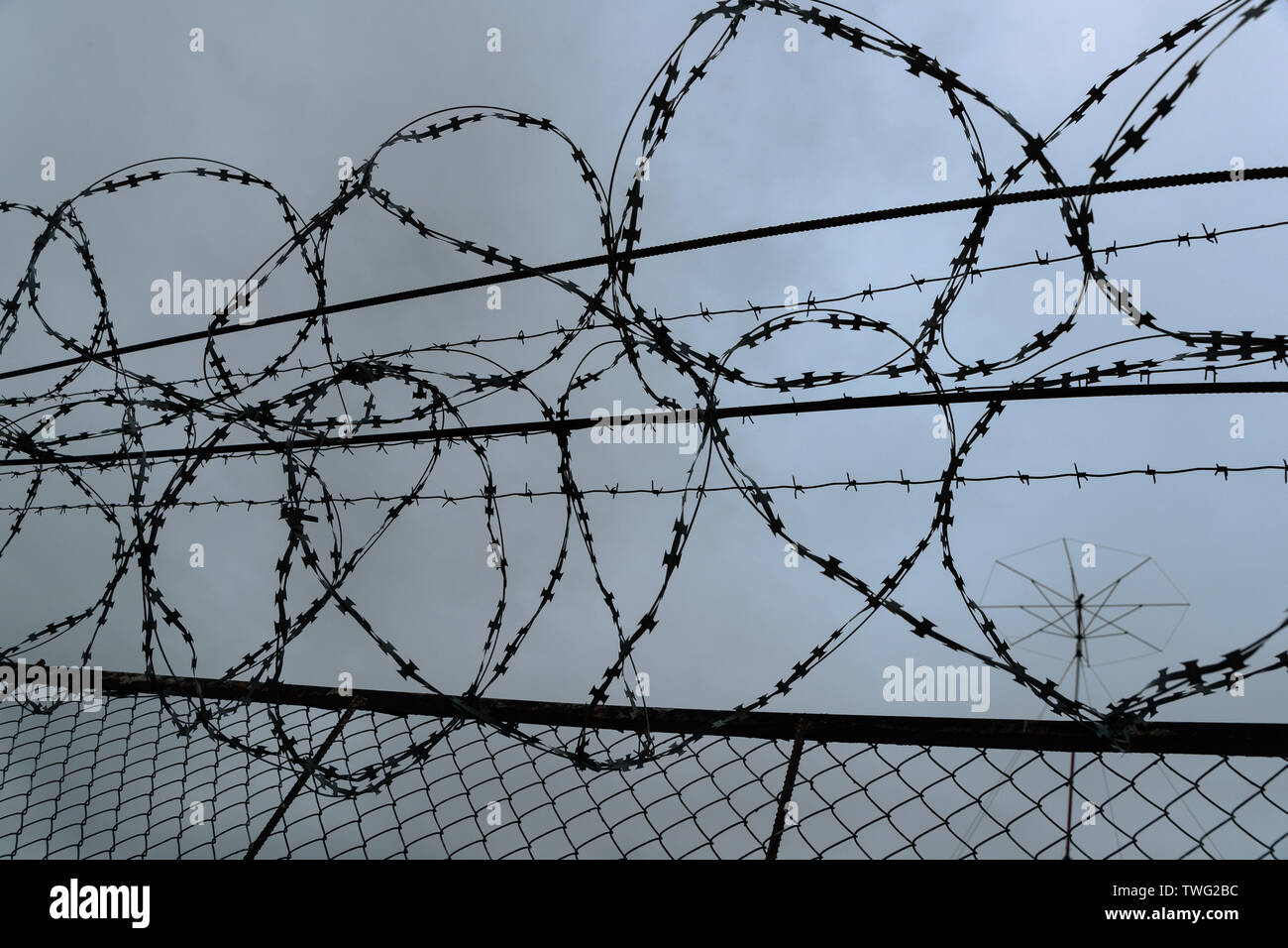 Filo spinato sulla recinzione in tempo nuvoloso Foto Stock