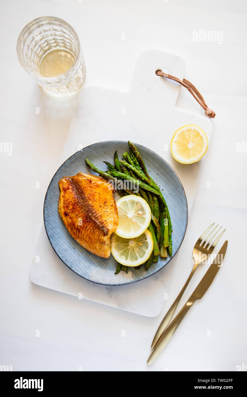 Arrosto di tilapia pesce con asparagi su una piastra di ceramica. Una sana dieta mediterranea il pranzo o la cena. Vista superiore, piatto laici. Foto Stock