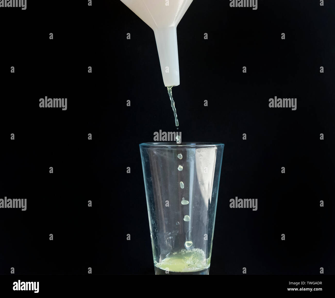 Il succo di mela scende da un imbuto di bianco in un bicchiere di vetro Foto Stock