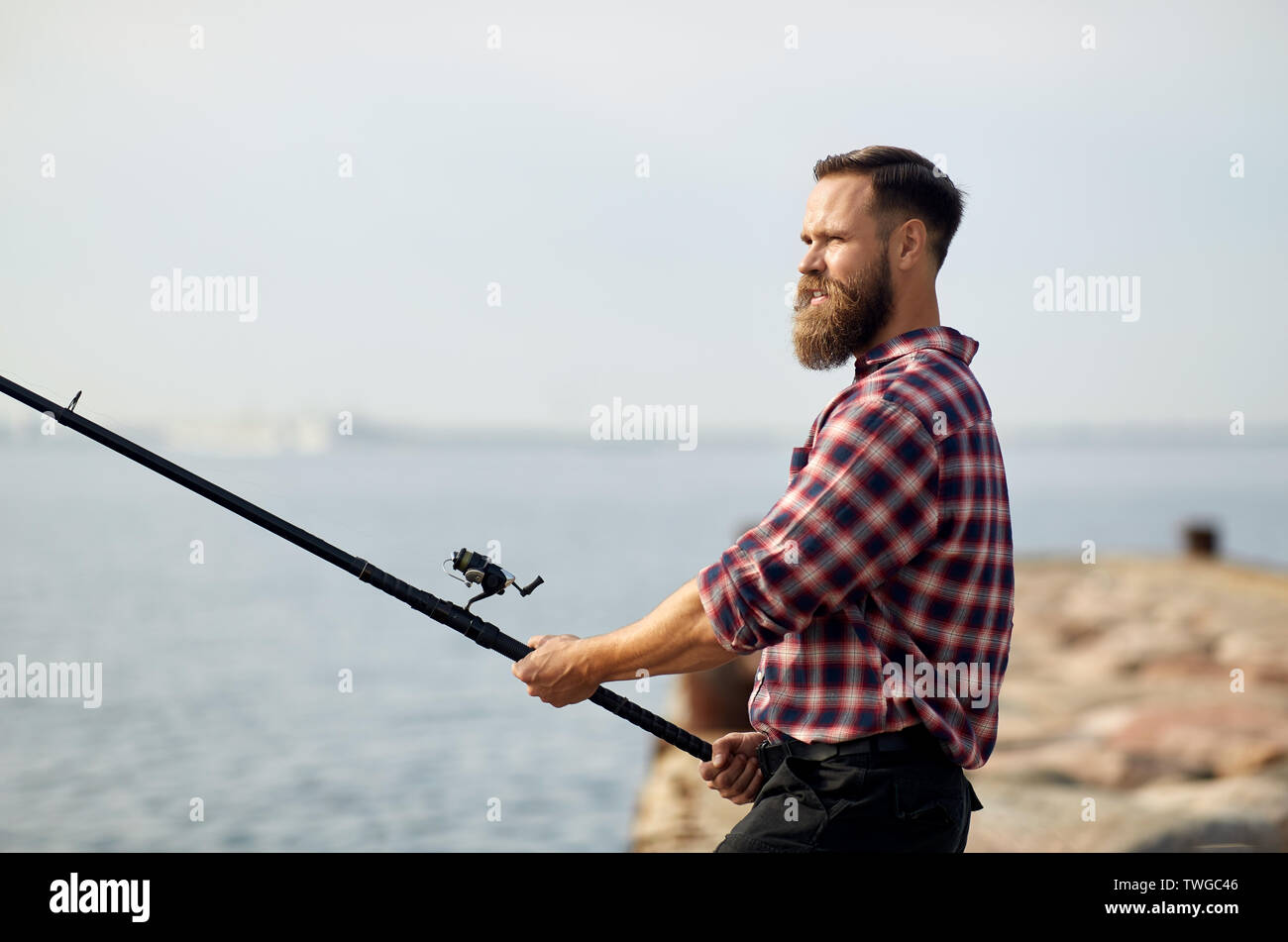 Barbuto pescatore con canna da pesca sul molo in mare Foto Stock