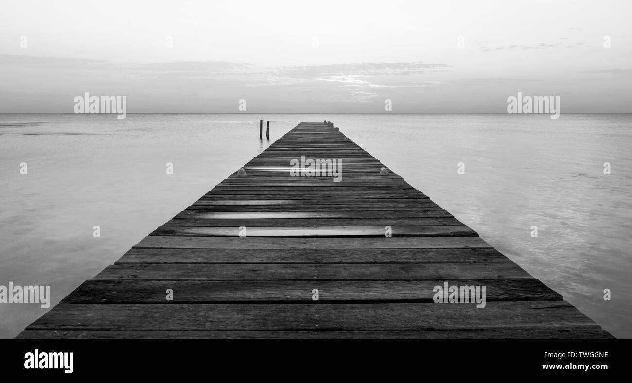 Alba di un pontile in legno che si stagliano all'oceano silenzioso in splendide in bianco e nero Foto Stock