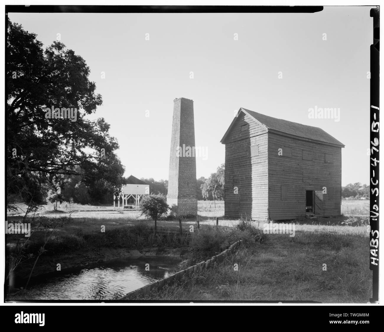Trebbiatura del riso mulino con camino. La sbramatura casa in background; canal in primo piano - Mansfield piantagione e la trebbiatura del riso Mill, U.S. Route 701 prossimità, Georgetown, Georgetown County, SC Foto Stock