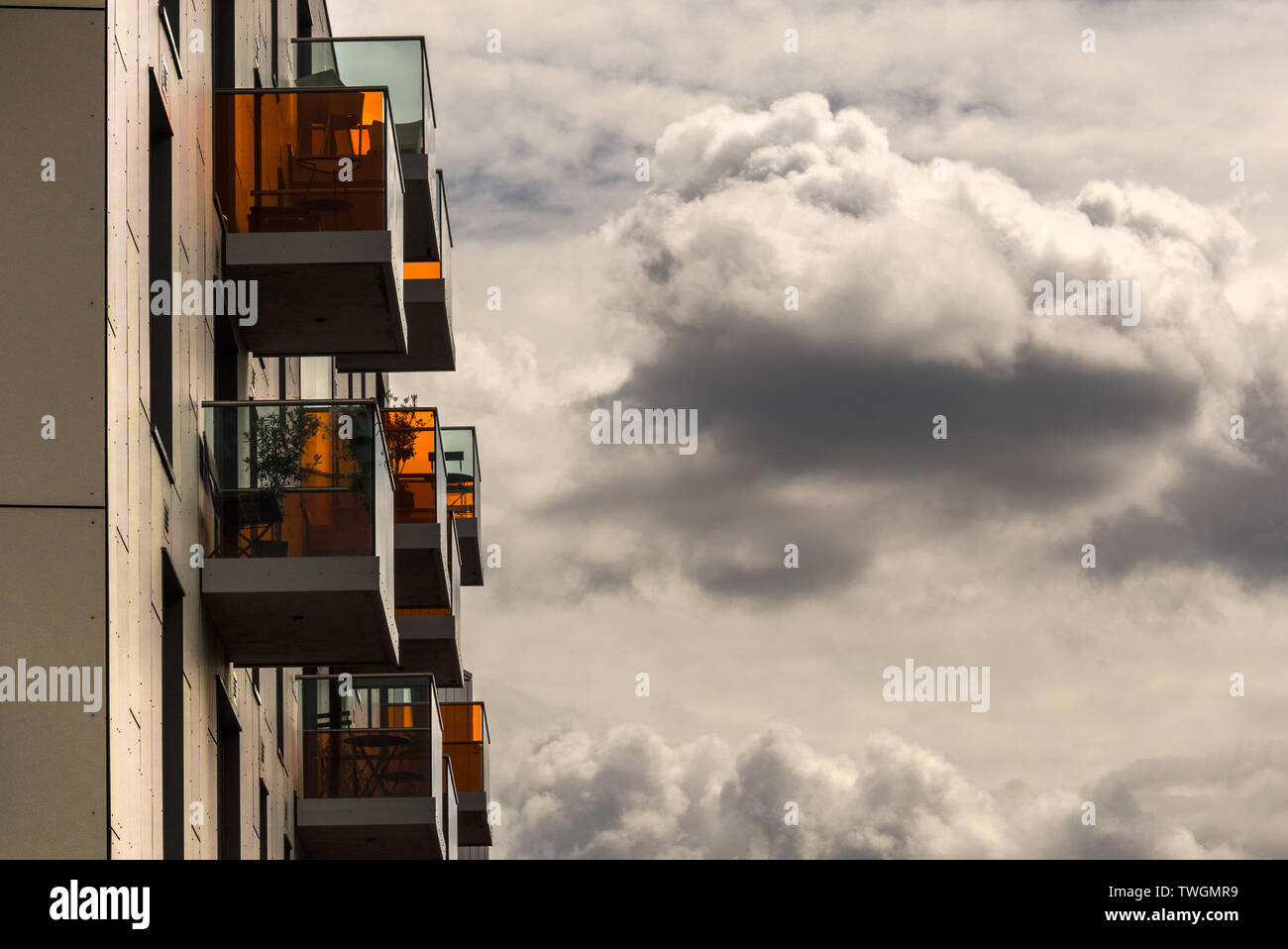 Gli appartamenti con balconi con vetro arancione contro un moody, cielo molto nuvoloso Foto Stock