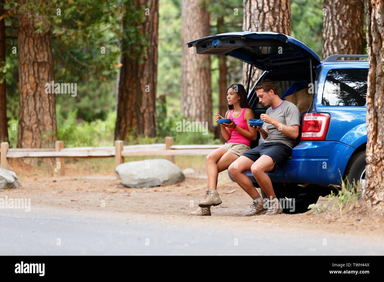 Giovane sulla strada auto viaggio nel mangiare nel bosco con pausa pranzo all'aperto sorridendo felice. Multirazziale, giovane donna asiatica, uomo caucasico persone in Yosemite National Park, California, Stati Uniti Foto Stock