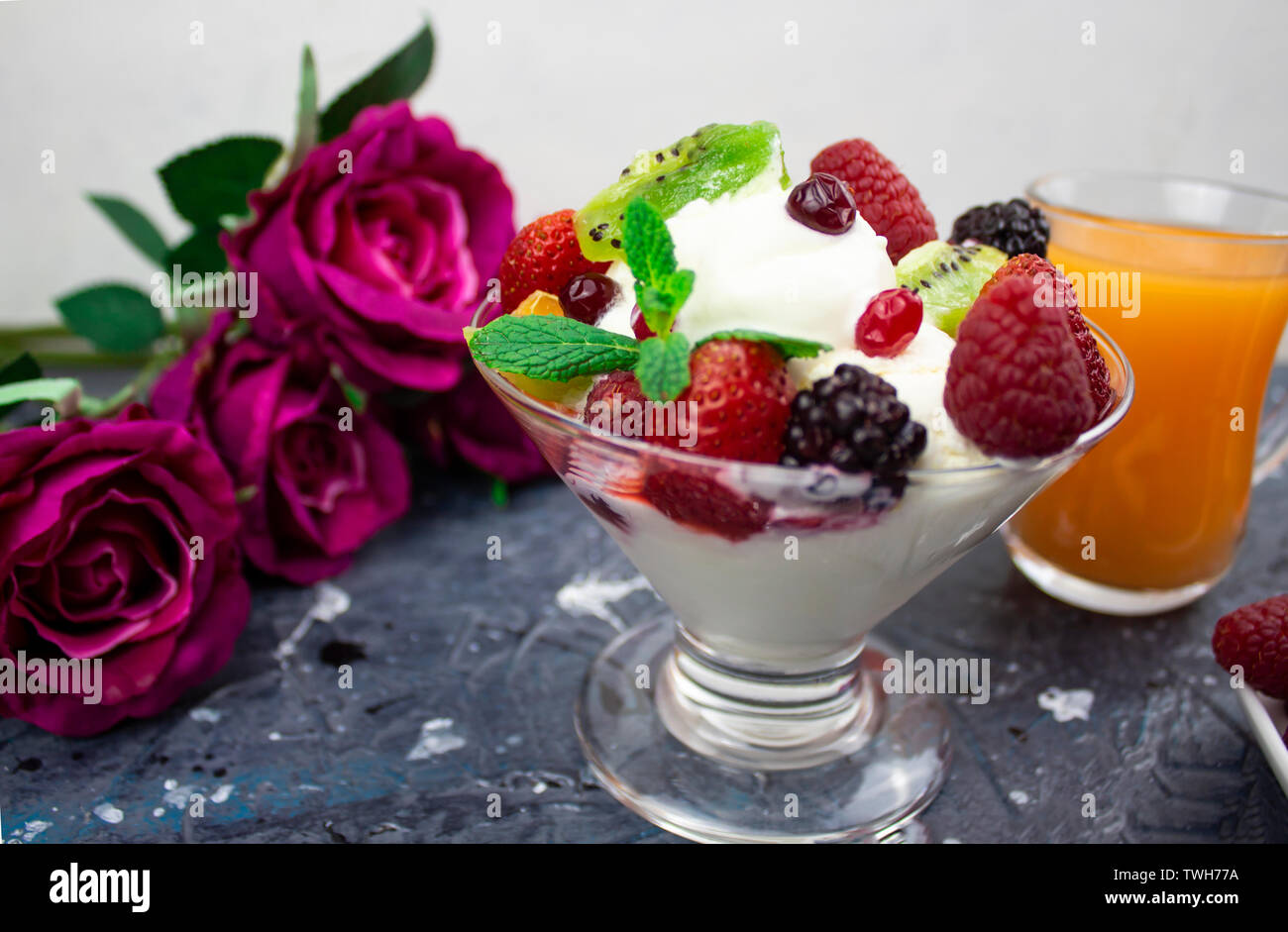 Il mandarino succo in un bicchiere, gelato alla crema con frutti di bosco sfondo. Rose Foto Stock