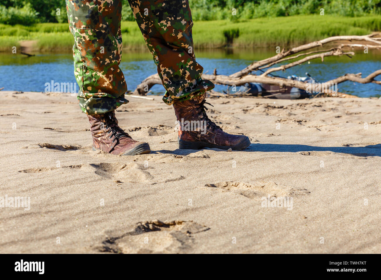 Uomini in piedi in stivali e Pantalone mimetico sulla sabbia di fiume Foto Stock