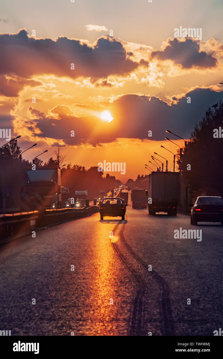 Autostrada con auto la guida al tramonto. Linea di orizzonte con il sole e nuvole temporalesche. Viaggi. Lunga distanza di frenatura. Messa a fuoco selettiva. Foto Stock