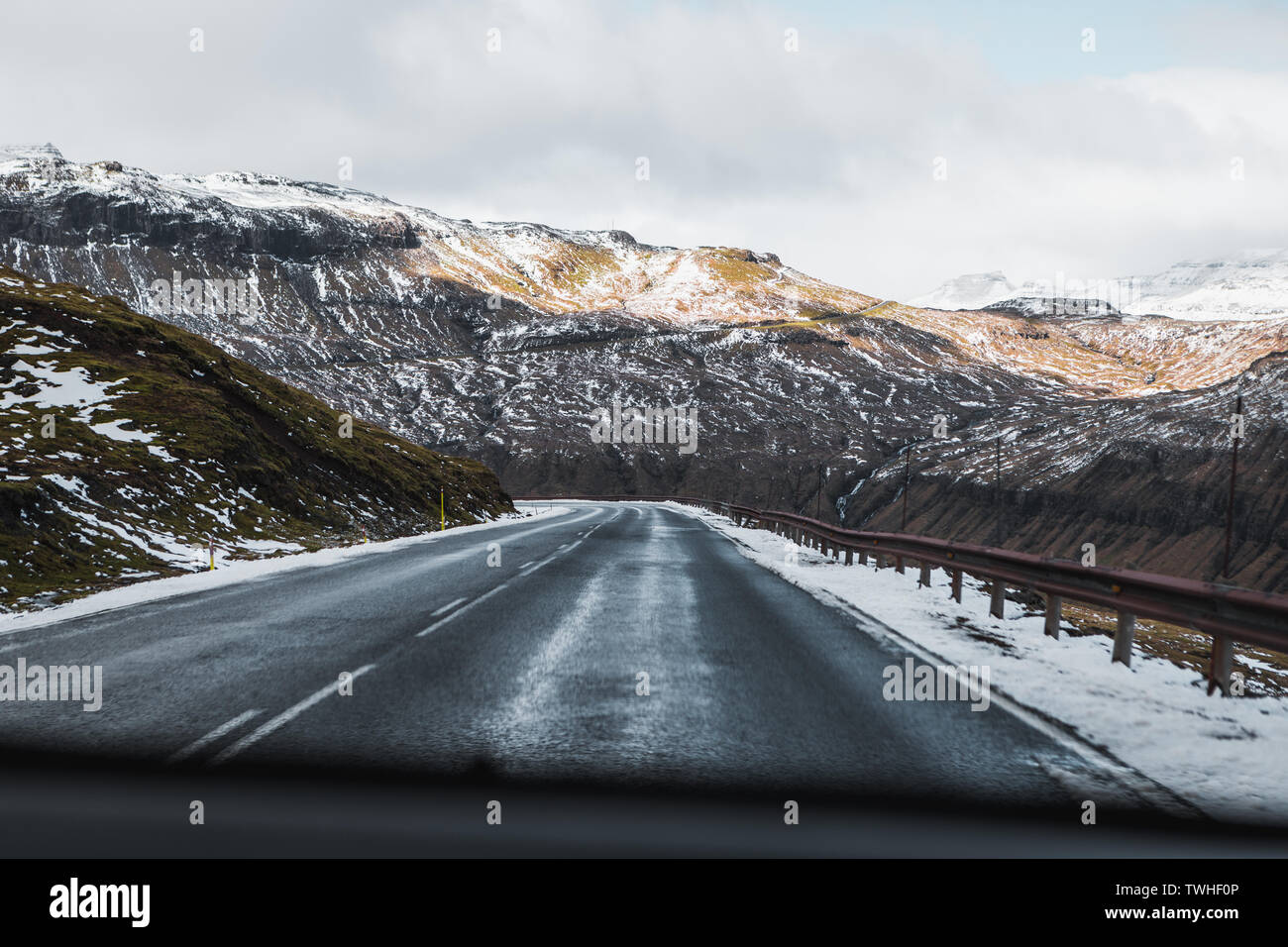 Road Trip opinioni sulle infinite strade su isole Faerøer con coperte di neve picchi di montagna, cielo azzurro e soleggiato durante la primavera (Isole Faerøer) Foto Stock