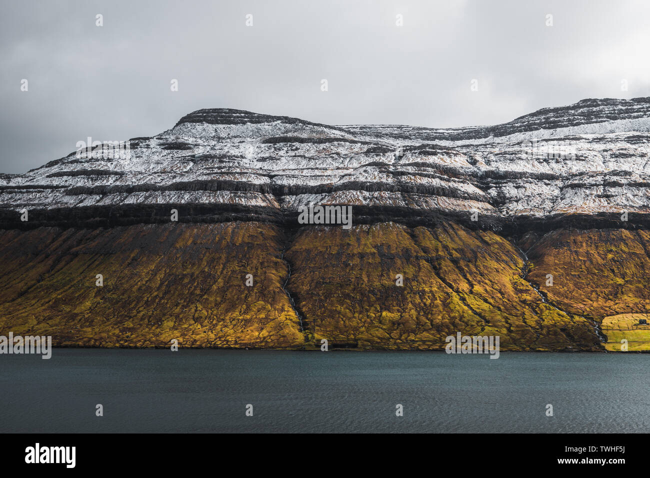 Vista sul tipico paesaggio delle isole Faeroeer con coperte di neve montagna con vasto prato arancione terra di fronte all'Oceano Atlantico (Isole Faerøer, Danimarca) Foto Stock