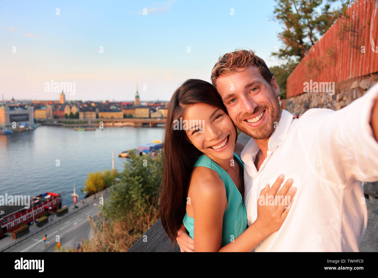 Giovane tenendo selfie ritratto di auto a Stoccolma. Candide scandinavo fresco uomo e donna asiatica guardando alla città vecchia cityscape vista tramonto da Monteliusvagen affacciato su Gamla Stan, la vecchia città. Foto Stock