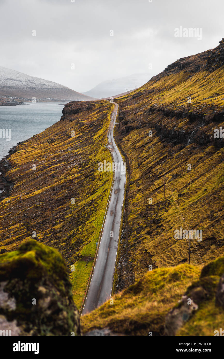 Lunga strada stretta che conduce verso la cascata di Fossa su isole Faerøer come individuato durante la primavera con vegetazione lussureggiante e arance (Isole Faerøer) Foto Stock