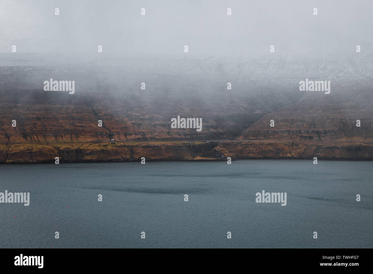 Moody tipico paesaggio delle isole Faeroeer come si vede dalla fossa cascata con nebbia bassa appesi nelle montagne di fronte al blu scuro del mare (Isole Faerøer) Foto Stock