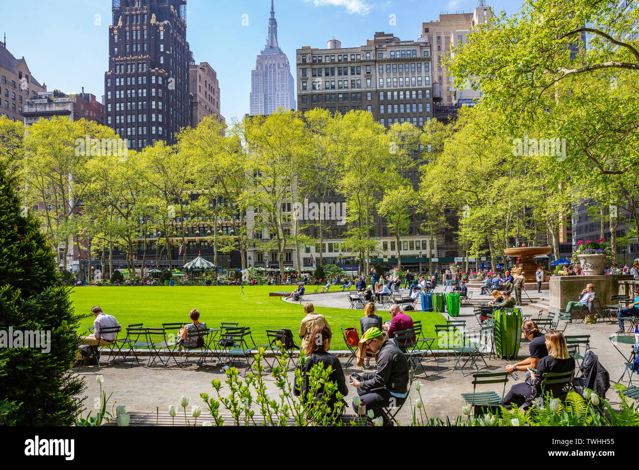 New York Manhattan Stati Uniti, Maggio 2nd, 2019. Primavera in Bryant Park. Persone rilassante, prato verde e alberi, cielo blu chiaro e grattacieli bac Foto Stock