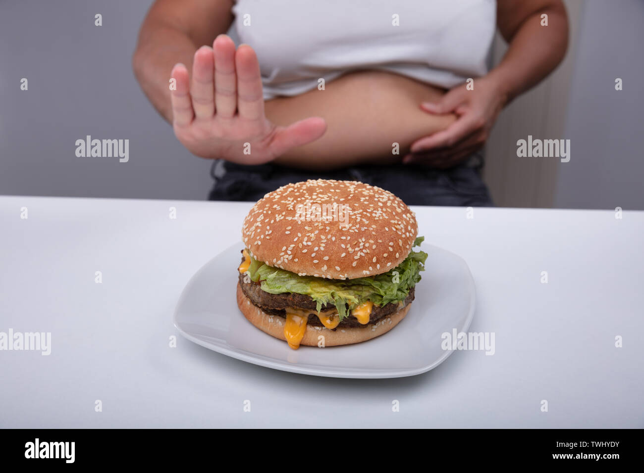 La sezione centrale del sovrappeso donna mostra nessun gesto di Hamburger sulla piastra al di sopra della tabella Foto Stock