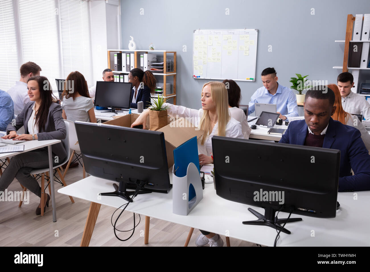 Gli imprenditori Guardando sorridente nuovo dipendente Disimballaggio Box con effetti personali in ufficio Foto Stock