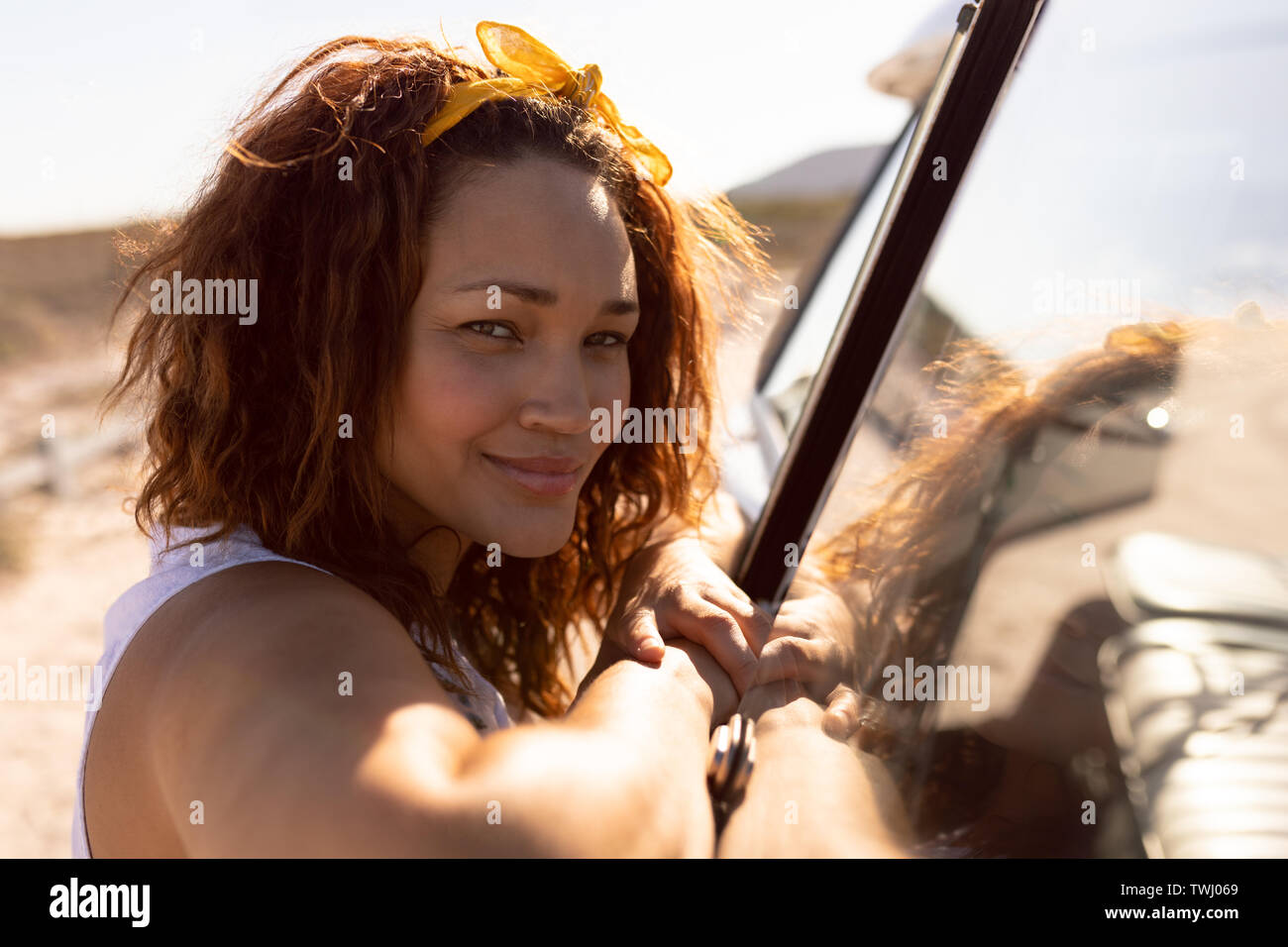 Donna birazziale appoggiata alla porta dell'auto, sorridente in spiaggia Foto Stock