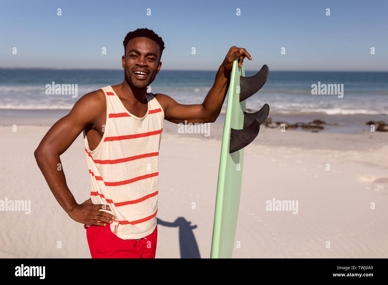 Uomo in piedi con la tavola da surf in spiaggia al sole Foto Stock