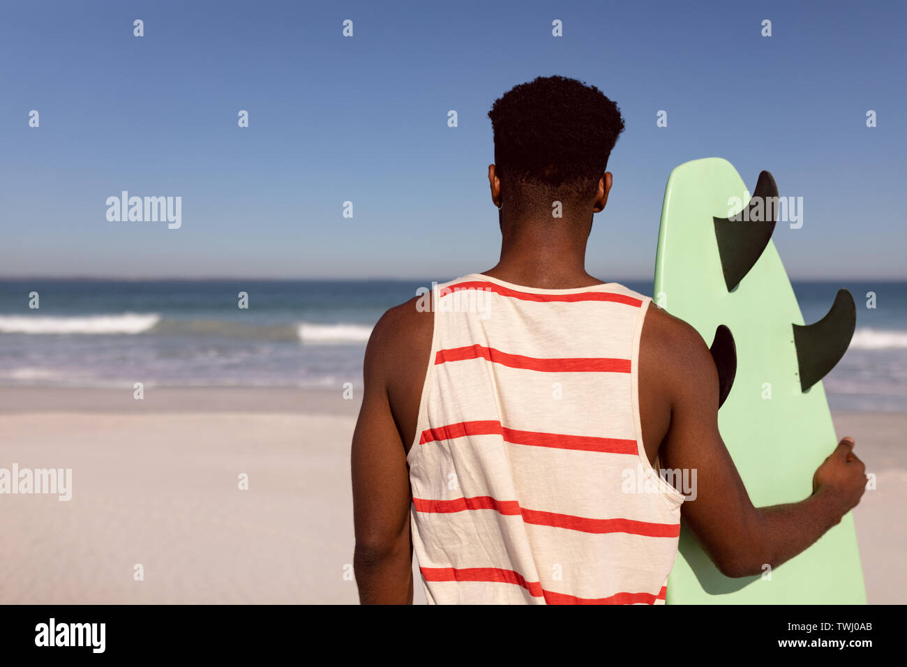 Uomo in piedi con la tavola da surf in spiaggia al sole Foto Stock