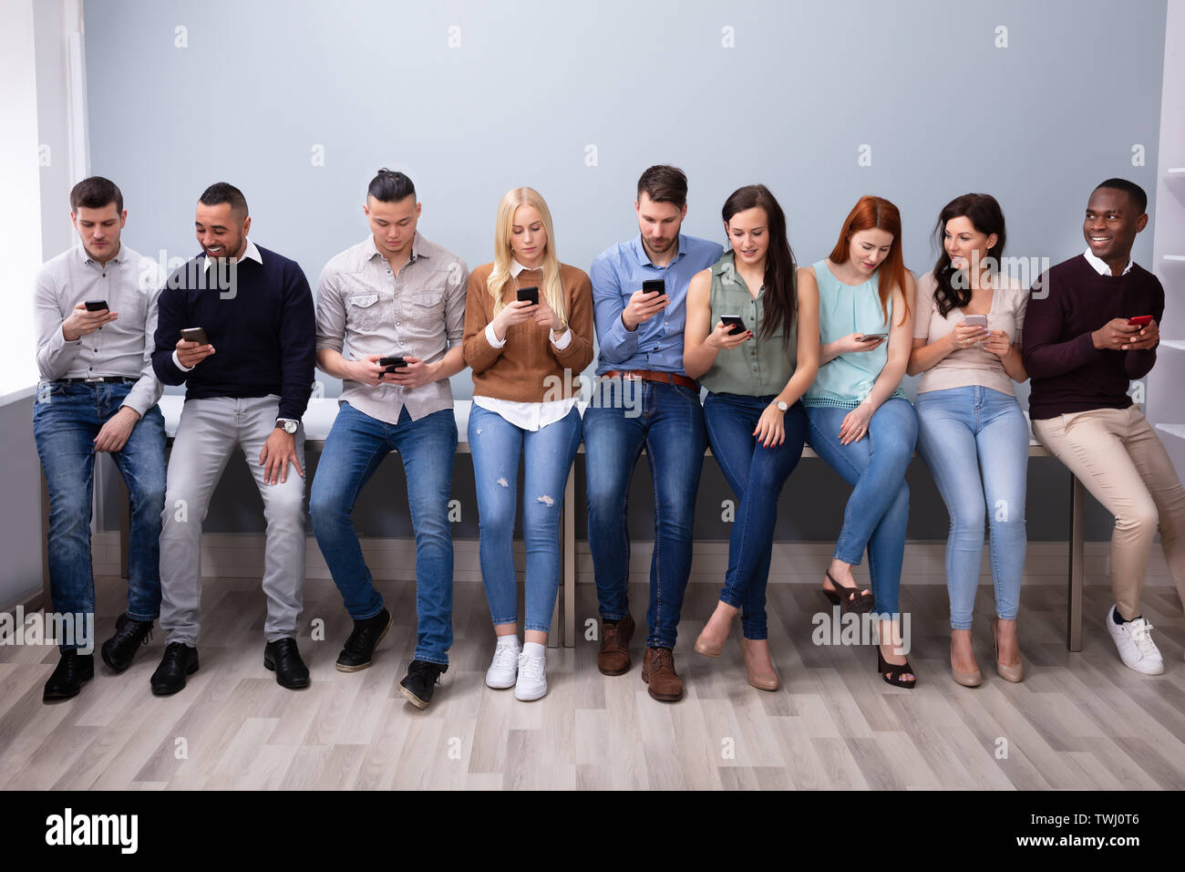 Multi-etnico Giovani appoggiata vicino a tavola in fila utilizza lo smartphone Foto Stock