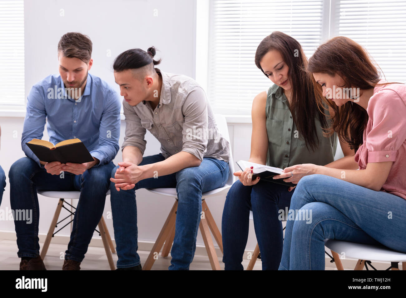 Gruppo di amici seduti insieme sulla sedia leggendo la Bibbia Foto Stock
