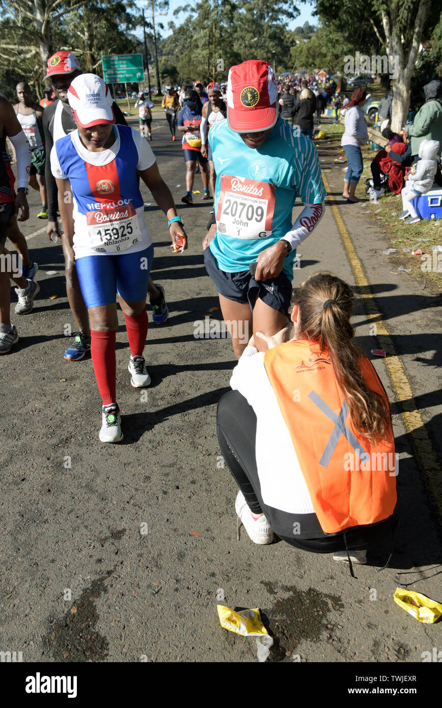 Durban, Sud Africa, donna runner guardando volontario soccorritore gamba massaggiante del concorrente maschio con crampi, 2019, compagni Marathon, persone sport Foto Stock
