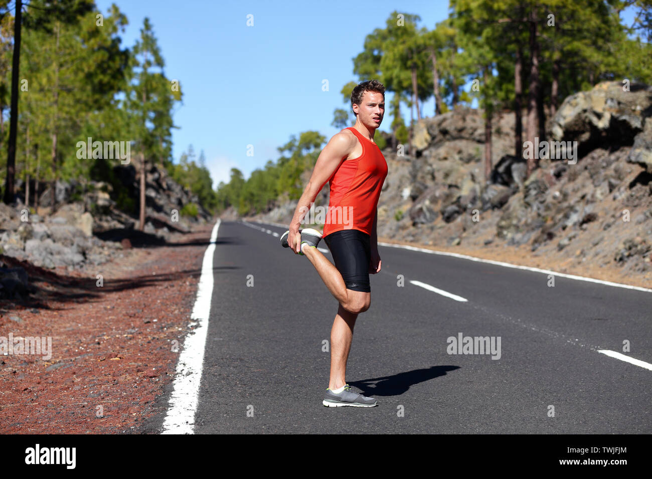 Runner uomo lo stiramento della coscia e gambe dopo aver eseguito su mountain Forest road a. Bel maschio caucasico modello fitness all'aperto. Foto Stock