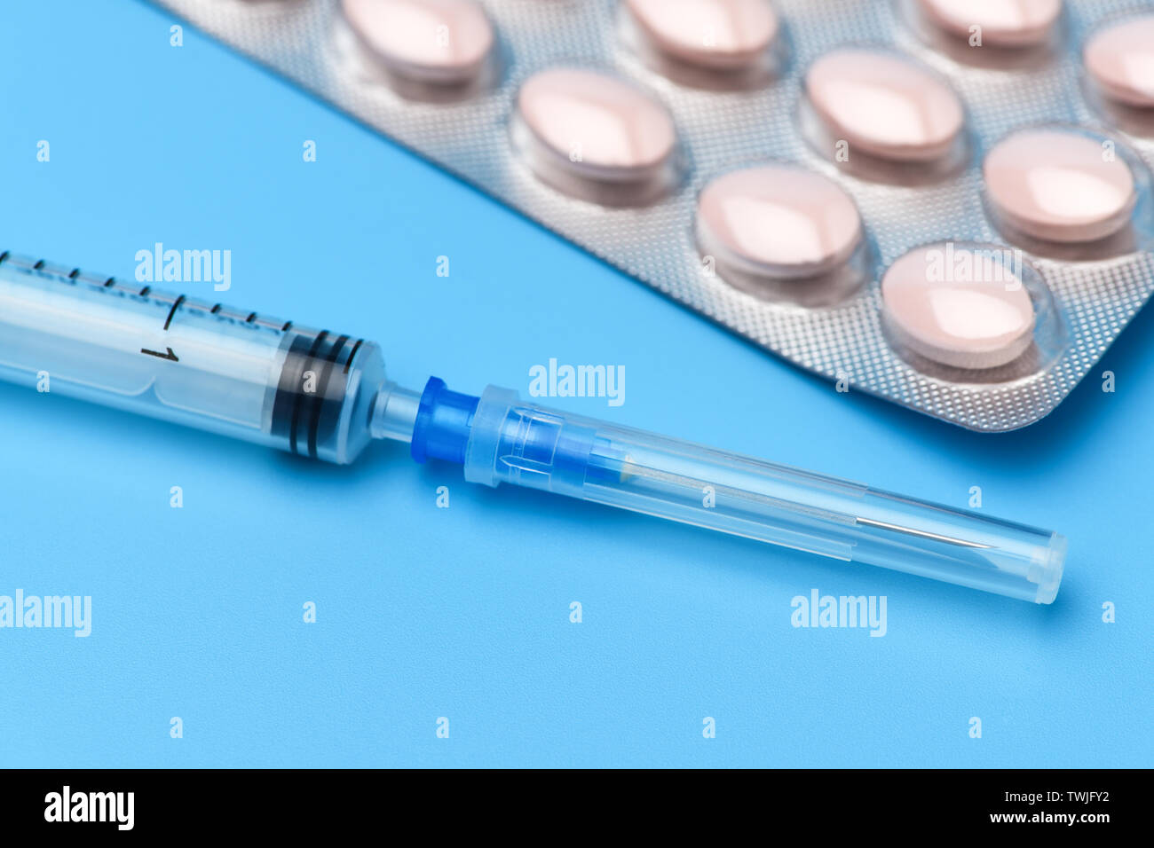 Molti compresse sono su sfondo blu in fondo è una siringa con una iniezione. Droghe e pillole di sfondo di prescrizione. Preparati farmaceutici Foto Stock