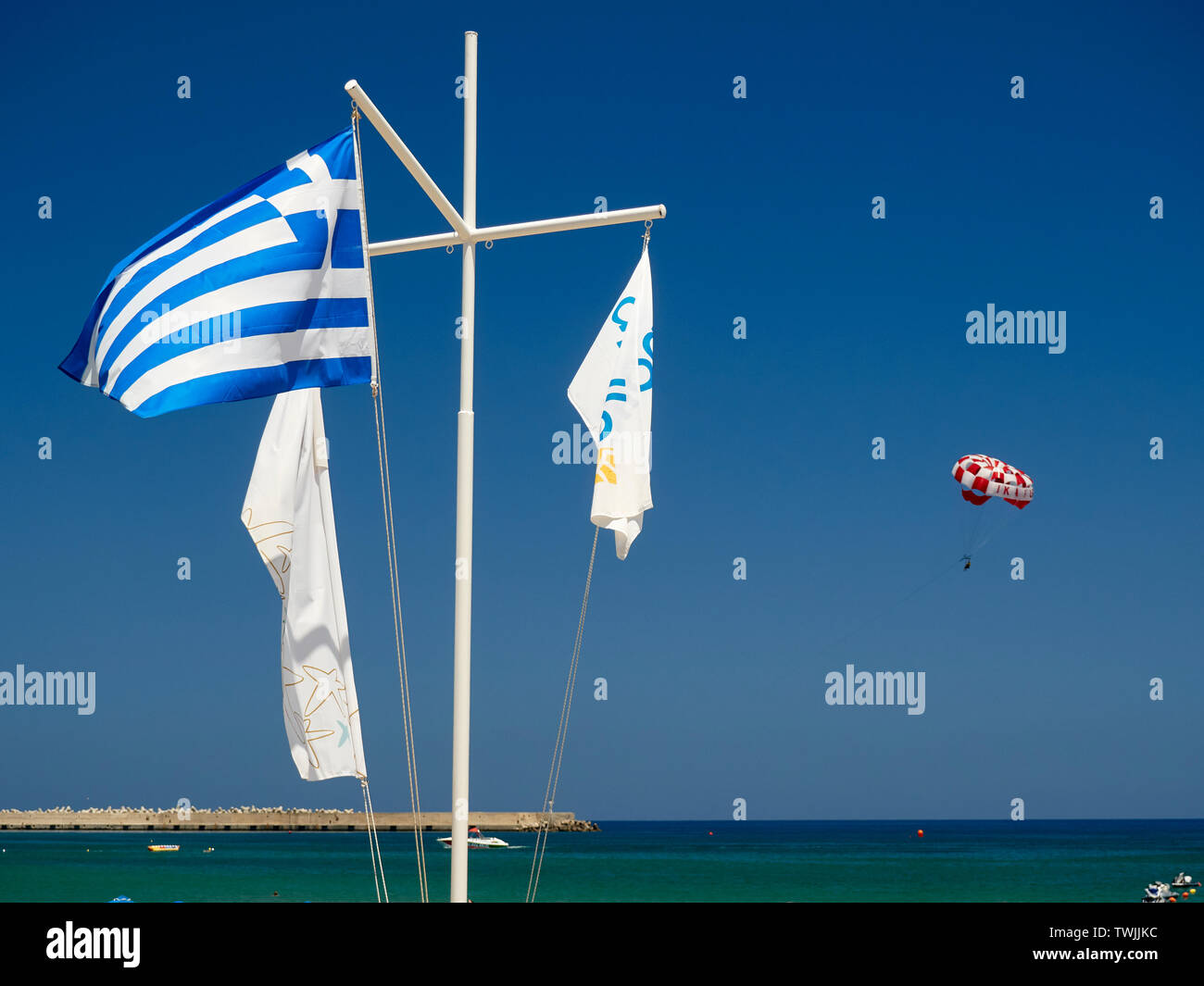 Bandiera Greca sulla spiaggia e parasailer in background, Rethymno (Rethymnon/Rethimno, Creta, Isole Greche, Grecia, Europa Foto Stock