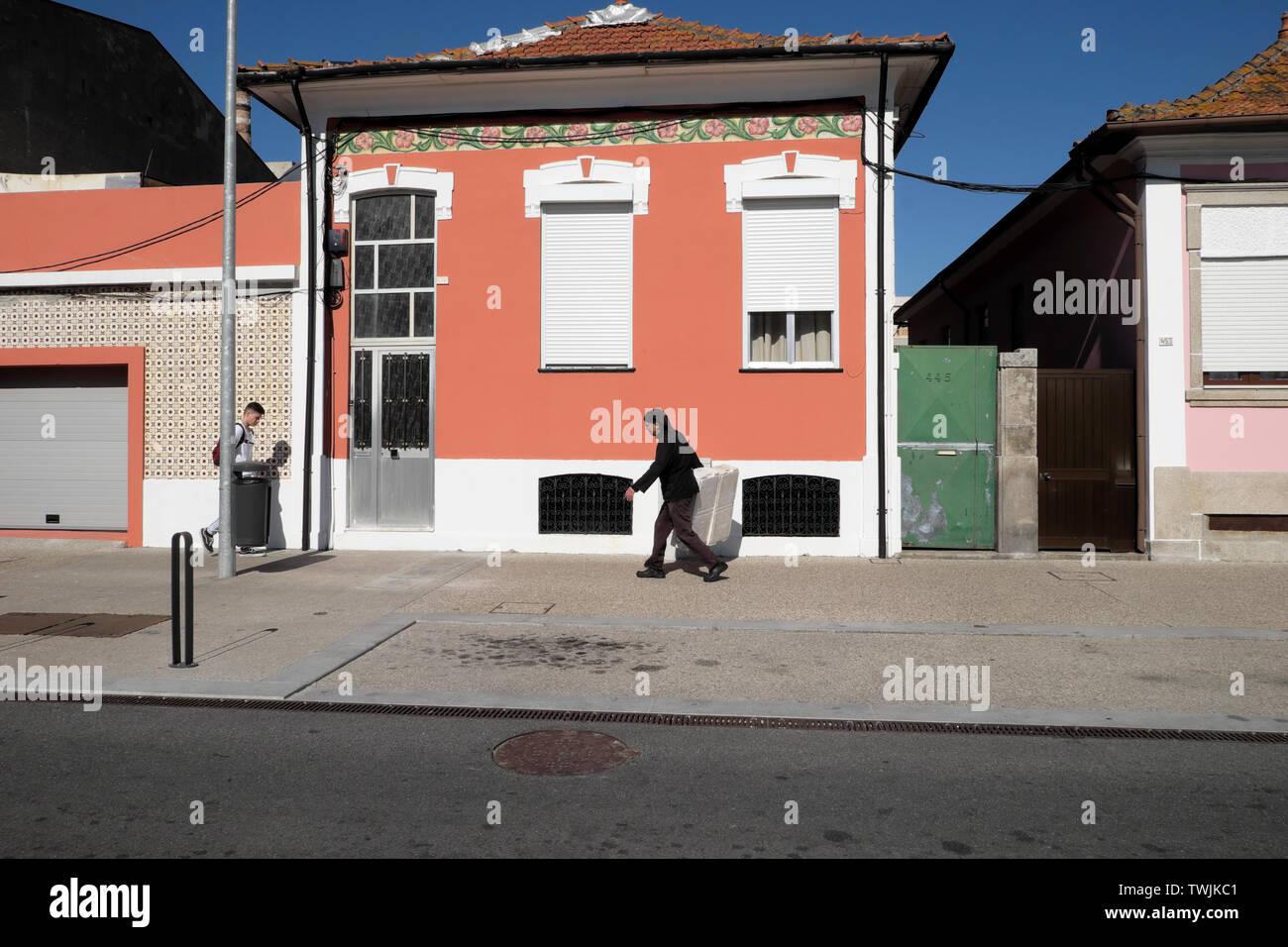 Consegna uomo a camminare lungo la strada passato una casa rosa con persiane che porta una scatola di polistirolo a Matosinhos Porto Portogallo, Europa UE KATHY DEWITT Foto Stock