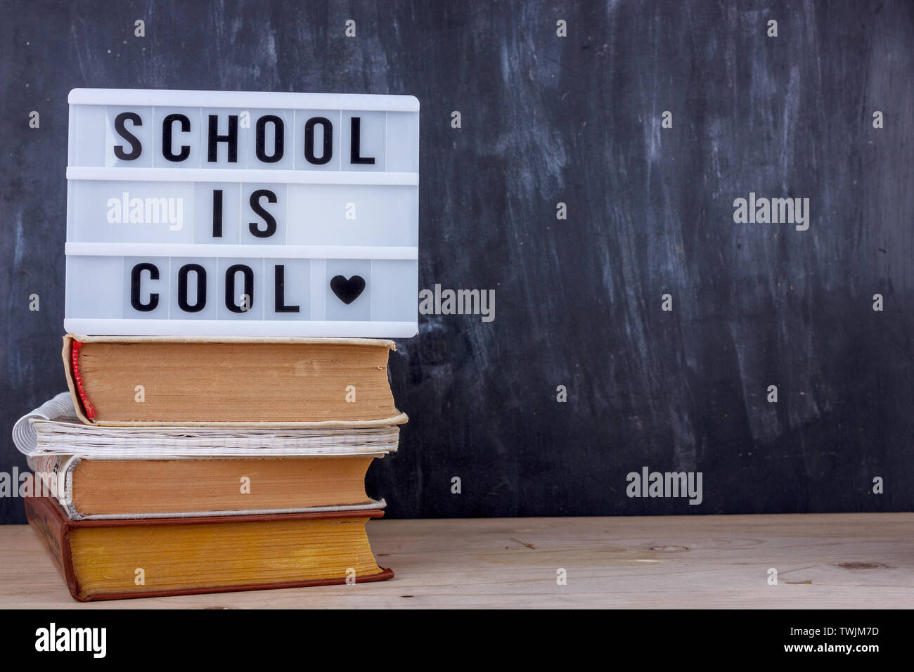 Lettering Scuola è cool sulla pila di libri. Nero scrivania sullo sfondo Foto Stock