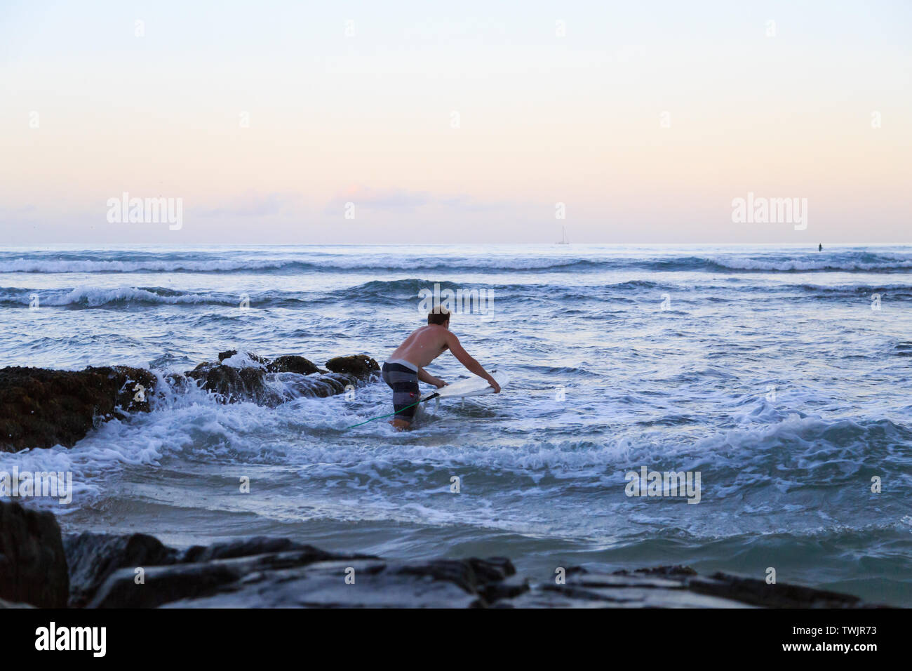 Un surfista maschio si pone fuori all'acqua prima del sorgere del sole in Kuhio Beach Park, Waikiki Hawaii. Foto Stock