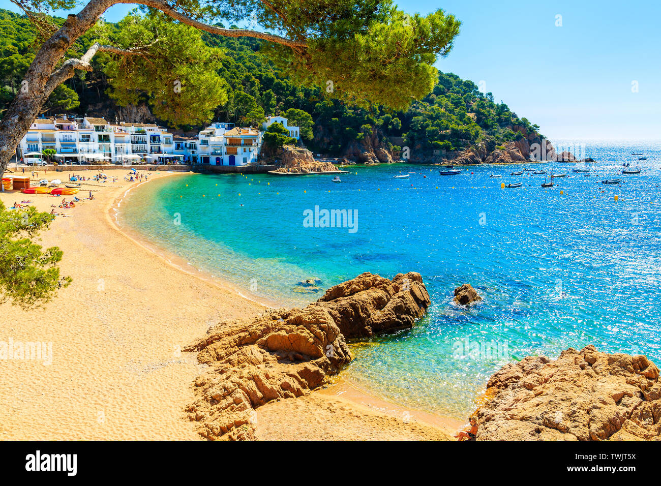 Giovane donna seduta su una roccia a incredibili sabbiosa spiaggia di Tamariu cittadina balneare, Costa Brava, Spagna Foto Stock