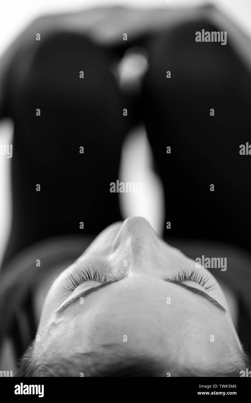 Un dark-haired brunette donna europea si trova sulla sua schiena facendo le ginocchia al petto porre o Apanasana, in bianco e nero verticale di close-up low-level vista. Foto Stock