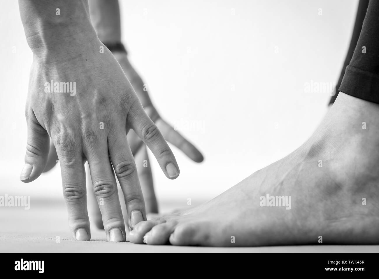 Close-up vista laterale delle mani e dei piedi di una giovane donna pratica Uttanasana o permanente di piegare in avanti lo Yoga posa, vista orizzontale Foto Stock