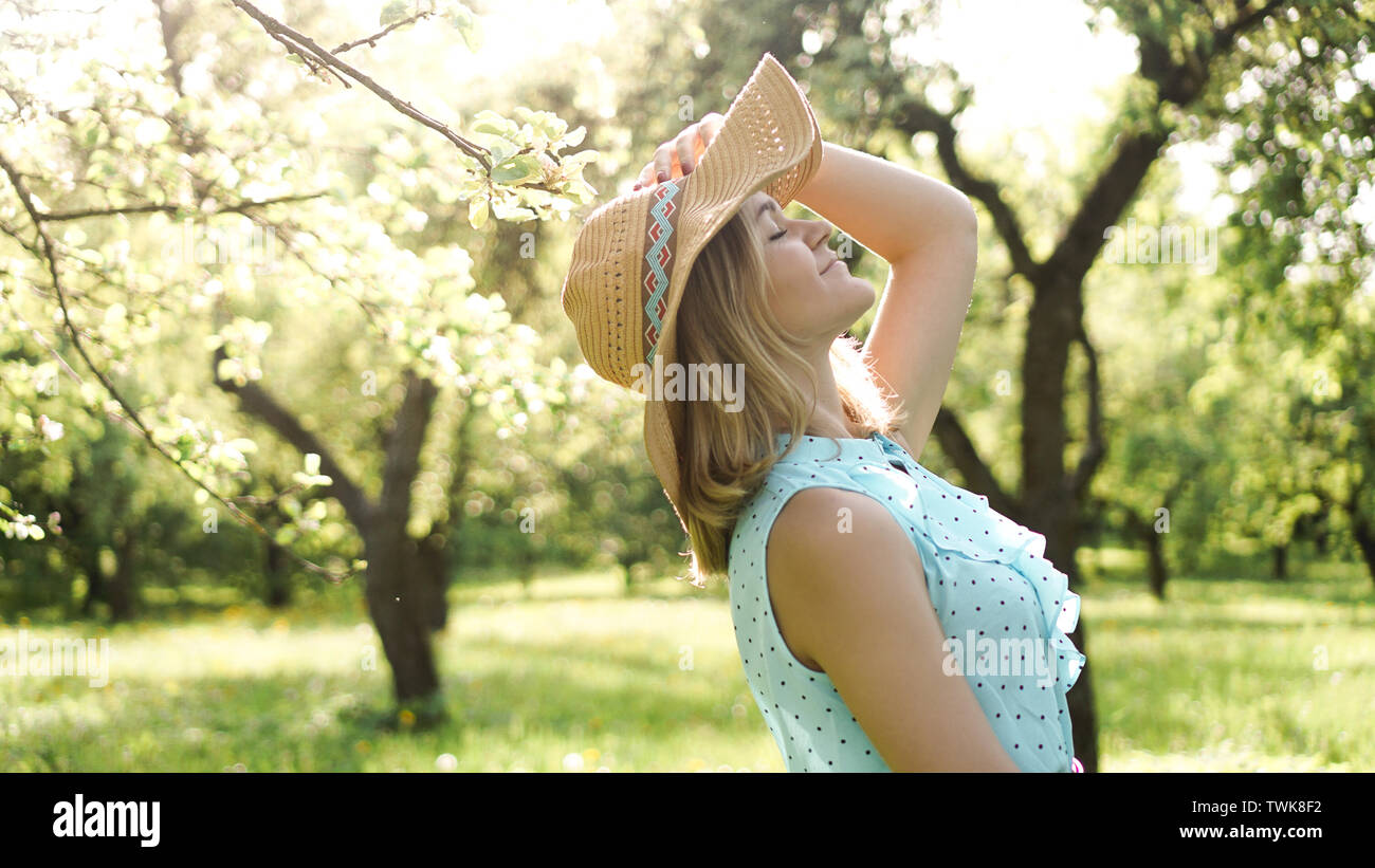 Felice giovane donna nel cappello di paglia nel giardino soleggiato Foto Stock
