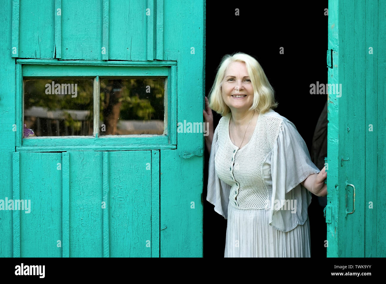 Anziani donna bionda in abito home apertura porta di ingresso. Foto Stock