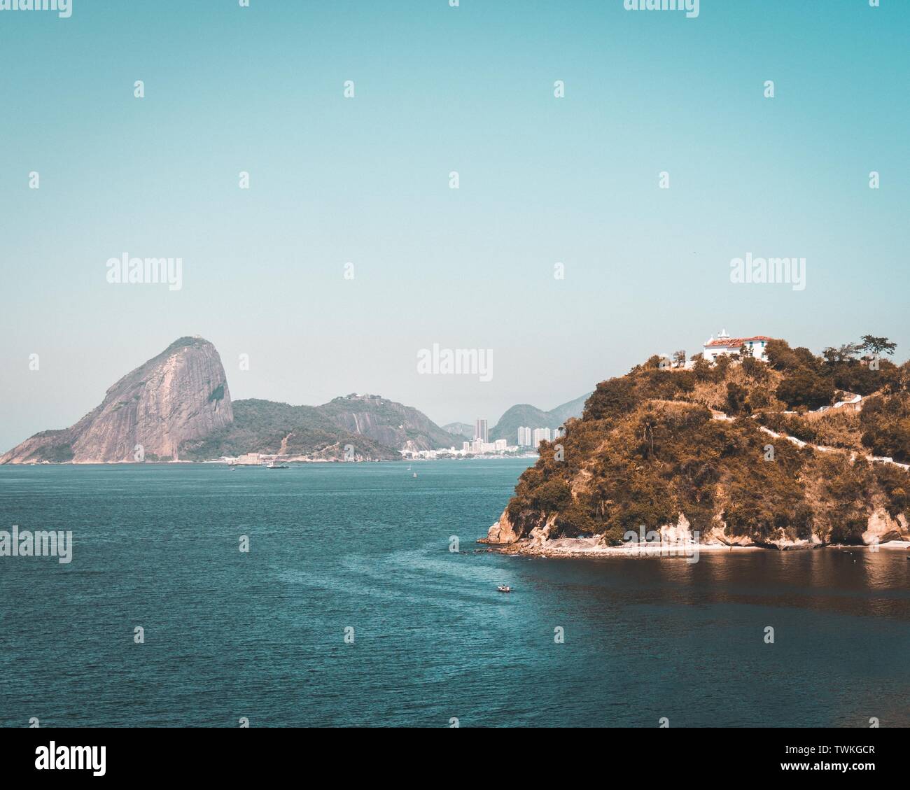Bellissimo scatto aereo del mare con un palazzo su una collina verde e alte rocce sullo sfondo Foto Stock