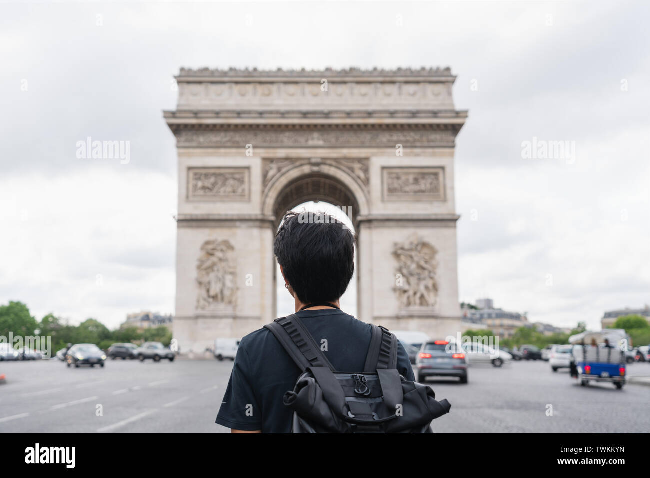 Un uomo con zaino guardando a Arc de Triomphe, famoso punto di riferimento e meta di viaggio a Parigi, Francia. Viaggiare in Europa in estate Foto Stock