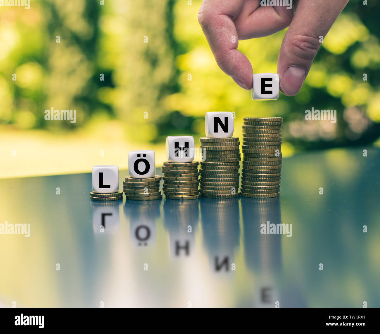 Concetto per l'aumento dei salari. Dadi formano la parola tedesca "Loehne' ('salari" in inglese) sulla parte superiore della crescente alte pile di monete. Foto Stock