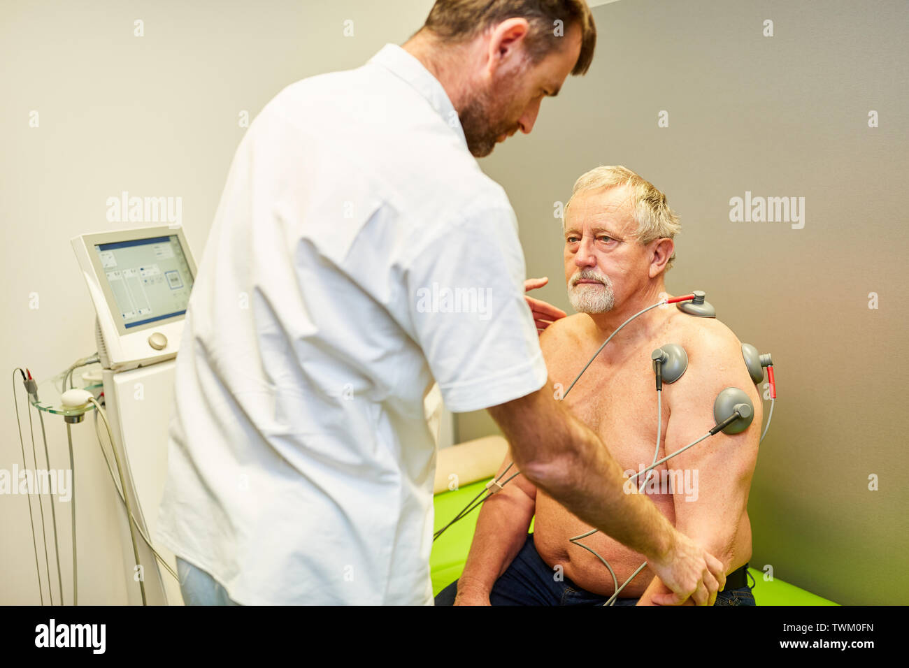 Ortopedico con senior uomo in elettroterapia per costruire il muscolo in ortopedia Foto Stock
