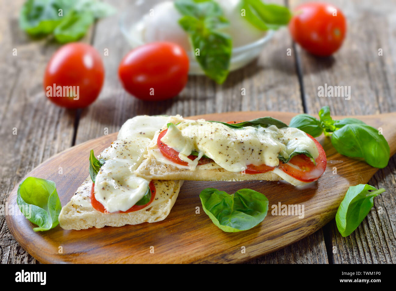 Panini al forno caprese con pomodoro, mozzarella e basilico, servita su un tagliere di legno Foto Stock