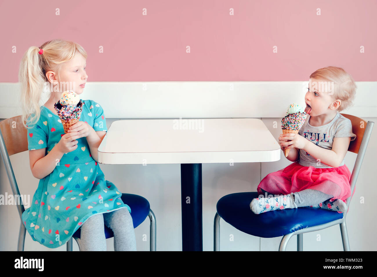 Stile di vita ritratto di due felice Caucasian carino adorabili bambini divertenti ragazze seduti insieme la vanteria vantando il loro gelato. Amore invidia gelosa sis Foto Stock